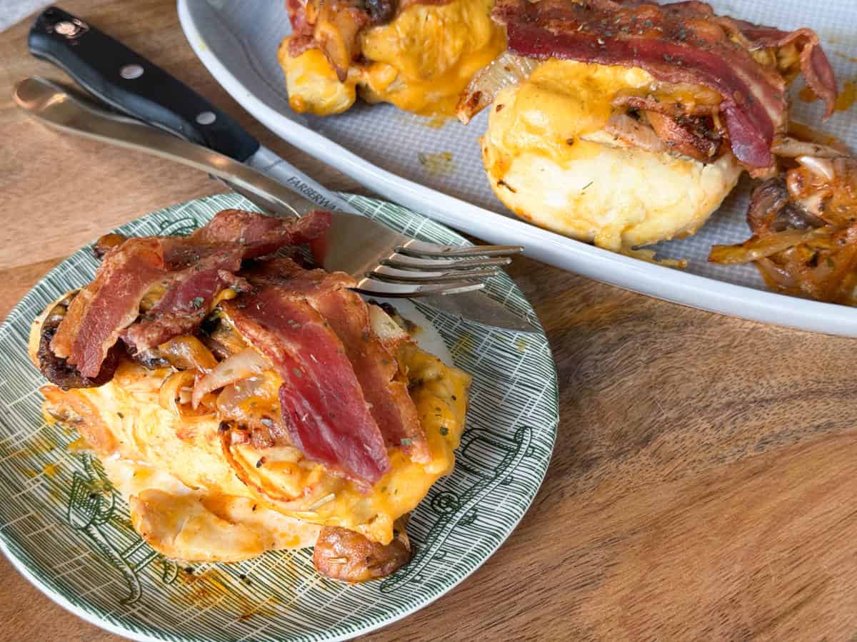Cheesy Cheddar Bacon Chicken Breasts served on a plate with a knife and fork on the side.