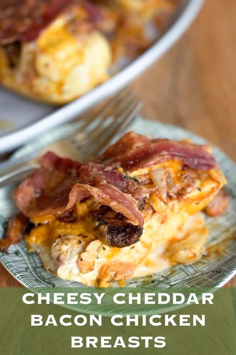 A close-up of a cooked cheesy cheddar bacon chicken breast served on a green and white plate with a fork resting on top. The background shows an additional portion of the same dish on a different plate. Text at the bottom reads, "Cheesy Cheddar Bacon Chicken Breasts.