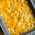 A baking dish filled with a baked casserole topped with a golden layer of melted cheese. The casserole appears to have a creamy base with visible pieces of pasta and other ingredients mixed in. The edges of the dish have a patterned design.