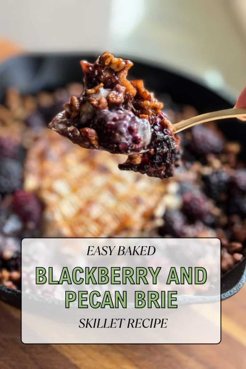 A hand holding a spoonful of blackberry and pecan mixture over a skillet with baked brie. A text overlay reads "Easy Baked Blackberry and Pecan Brie Skillet Recipe." The dish includes a baked brie topped with blackberries and pecans.
