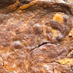Close-up view of a baked item with a marbled texture, displaying swirls of brown and orange color. The surface appears slightly cracked and golden brown, indicating baked goods that may include ingredients like chocolate and pumpkin.