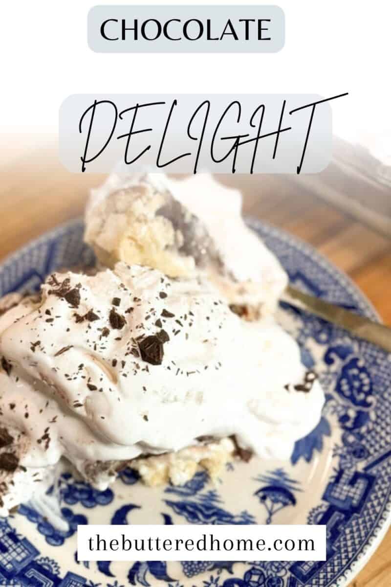 A blue and white patterned plate holds a slice of dessert topped with whipped cream and chocolate shavings. The background includes the text "Chocolate Delight" and "thebutteredhome.com." A fork is partially visible on the plate.
