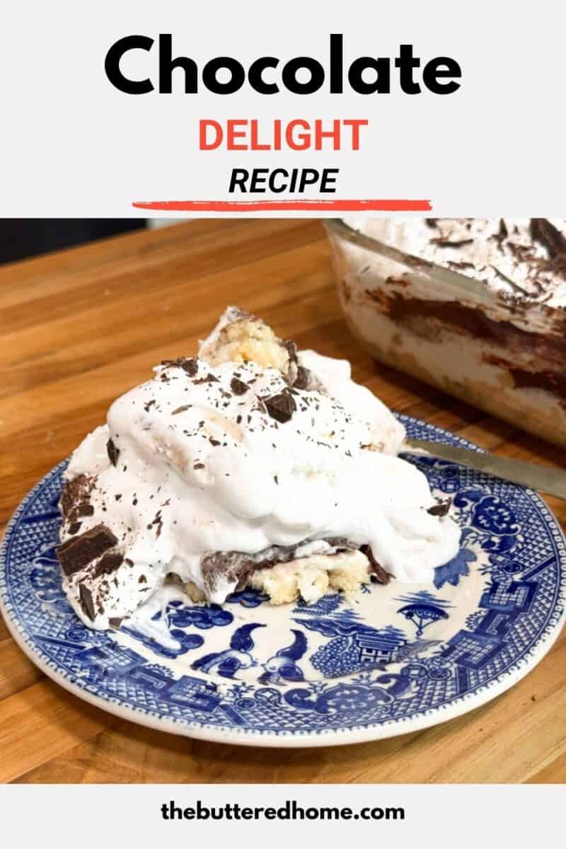 A slice of chocolate delight dessert with whipped topping and chocolate shavings is served on a blue and white patterned plate. The dessert dish on a wooden surface is partially visible in the background.