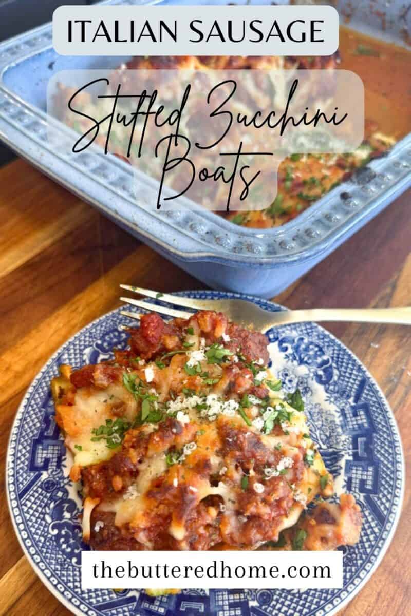 A plate of Italian sausage stuffed zucchini boats topped with cheese and herbs sits on a blue patterned plate. Behind it, a baking dish with more stuffed zucchini is partially visible. Text reads: "Italian Sausage Stuffed Zucchini Boats" and "thebutteredhome.com".