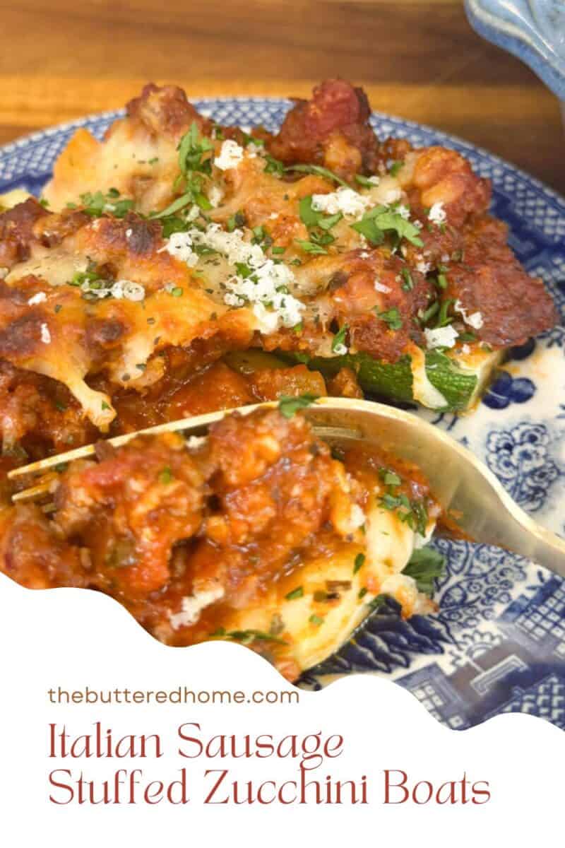 A plate with zucchini boats filled with Italian sausage, topped with tomato sauce and melted cheese. Garnished with chopped parsley and grated cheese. A spoon rests on the plate. Text reads: "thebutteredhome.com Italian Sausage Stuffed Zucchini Boats.