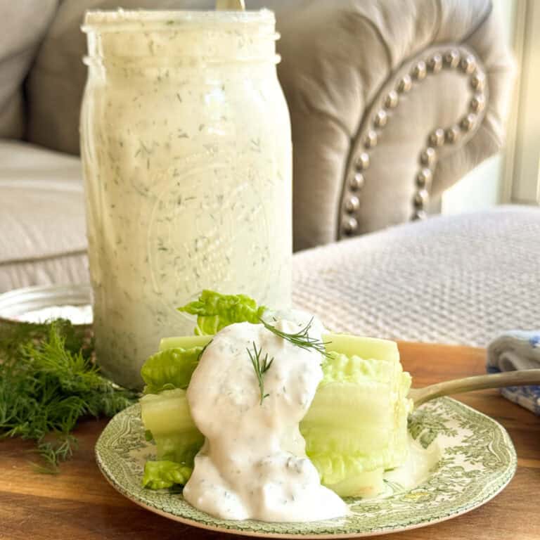 Romaine lettuce hearts on a decorative plate topped with ranch dressing and a dill sprig, with a large mason jar of ranch dressing in the background on a wooden surface.