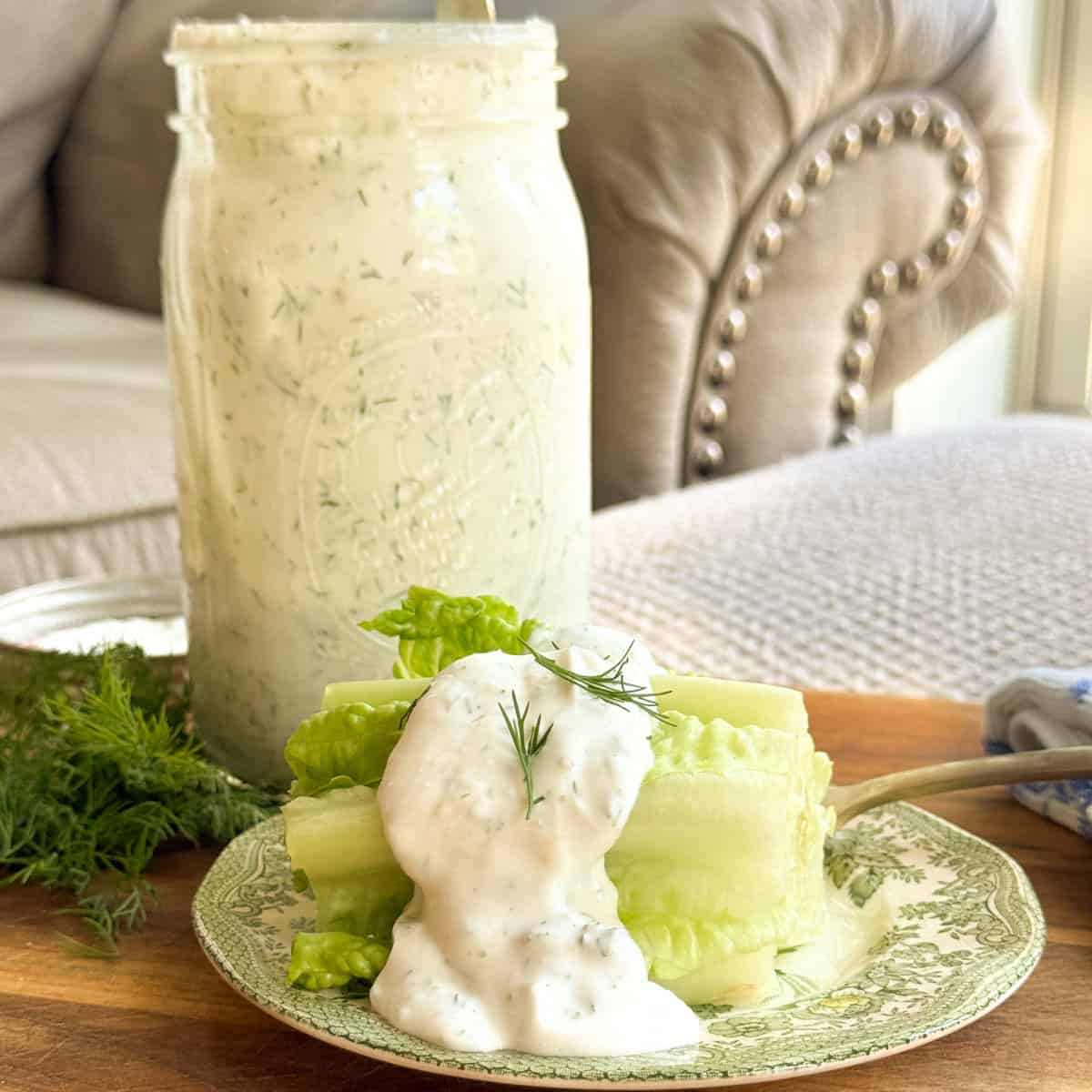 Romaine lettuce hearts on a decorative plate topped with ranch dressing and a dill sprig, with a large mason jar of ranch dressing in the background on a wooden surface.