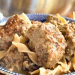 A blue patterned bowl filled with meatballs and wide egg noodles, covered in a creamy brown sauce. The dish appears freshly cooked with a rich, textured appearance.
