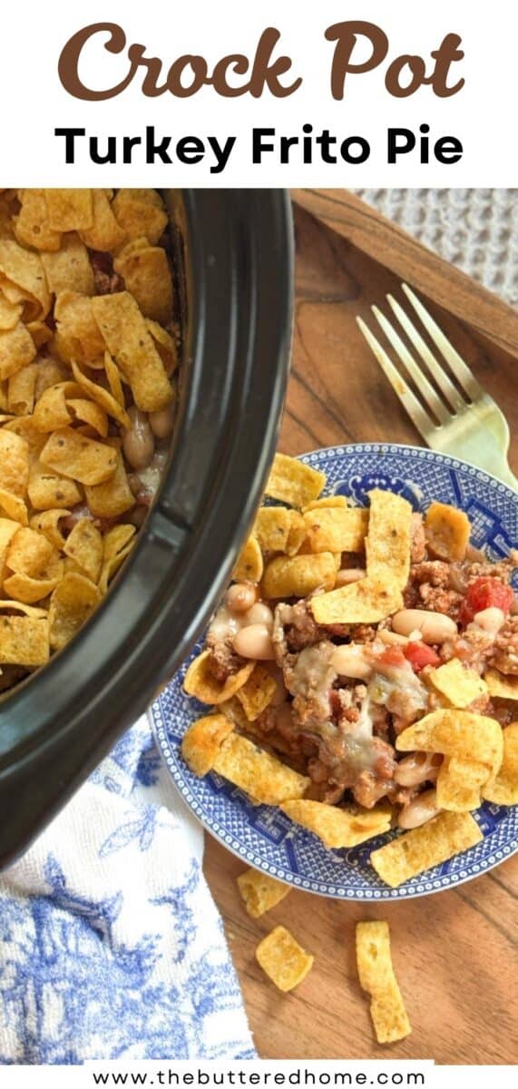 A blue plate holds a serving of turkey Frito pie with ground turkey, beans, tomatoes, and corn chips, next to a slow cooker filled with more of the dish. A fork rests on a wooden board beside the plate.