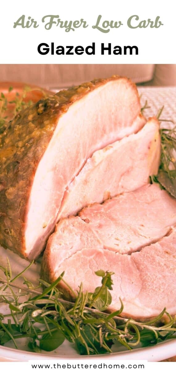 A sliced glazed ham garnished with fresh herbs is shown on a white plate. The image is labeled "Air Fryer Low Carb Glazed Ham" with a website address at the bottom: thebutteredhome.com.