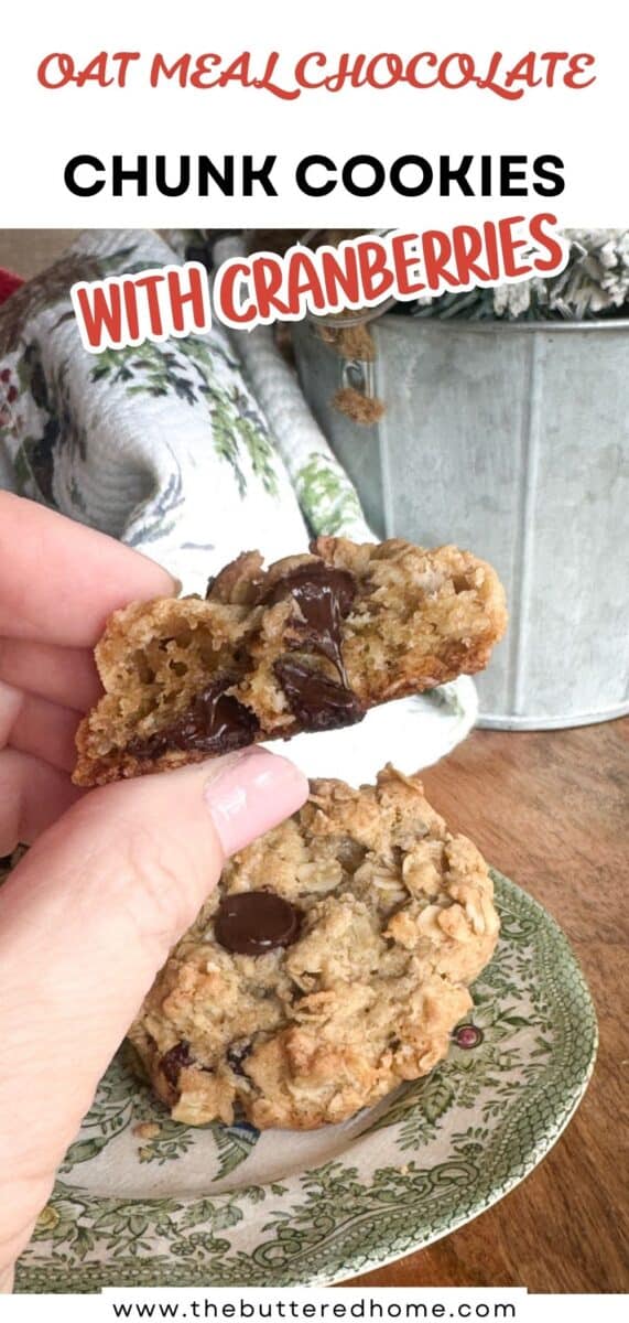 A hand holds half of an oatmeal chocolate chunk cookie with cranberries above a green-patterned plate containing another whole cookie. Text on the image reads, “Oatmeal Chocolate Chunk Cookies with Cranberries.”.