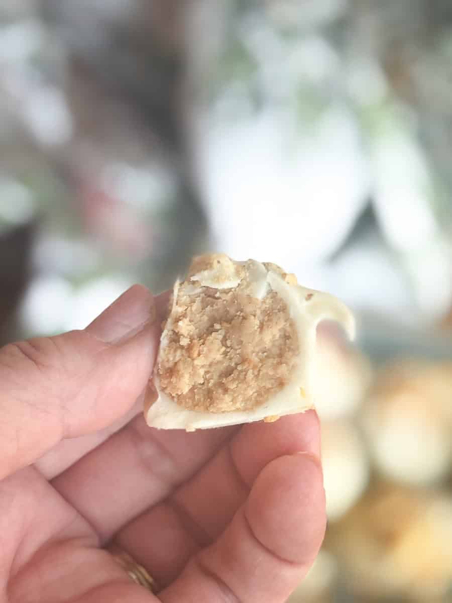 A hand holding a cut dumpling, showing its crumbly, beige filling inside a thin, white wrapper. The background is softly blurred.